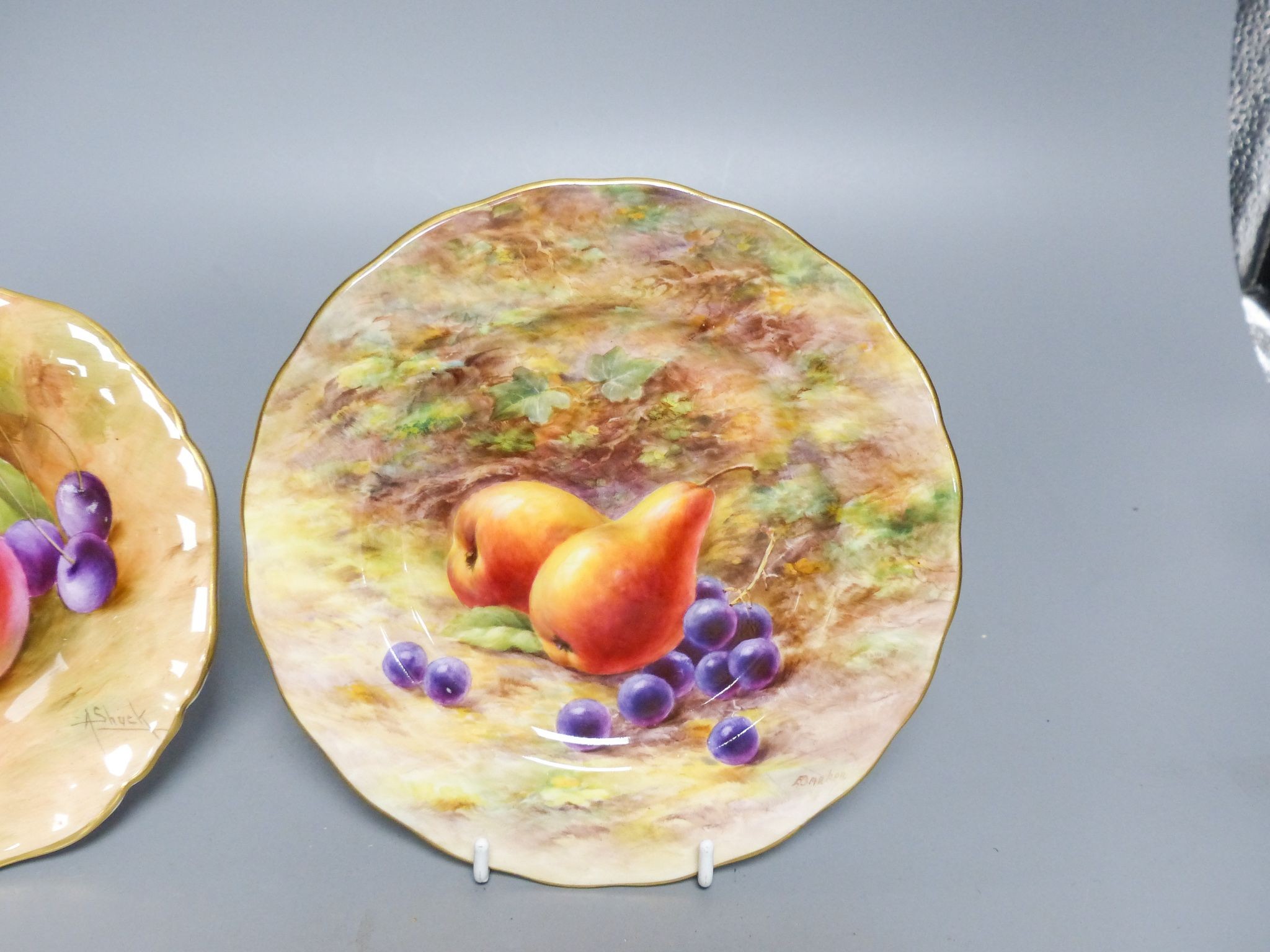 A Royal Worcester fruit painted pedestal dish signed A Shuck and a similar plate signed E Barnes, early 20th century, 14.3 and 16cm